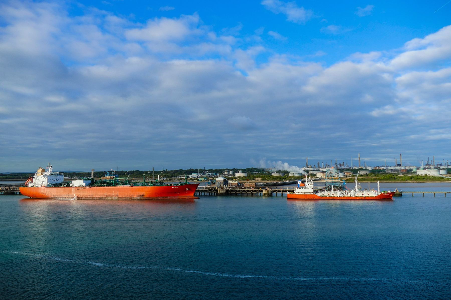 A tanker and an LPG carrier alongside a terminal, with a refinery behind